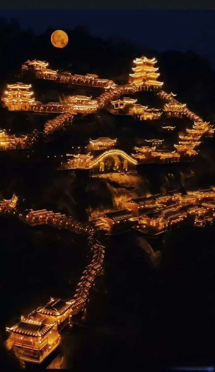 Wangxian Valley illuminated at night with warm golden lights cascading down the cliff face, creating a magical vertical village of light