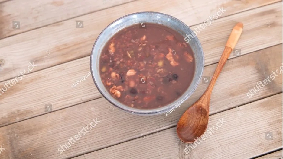 A steaming bowl of Laba porridge topped with dried fruits, nuts, and red dates in a traditional ceramic bowl