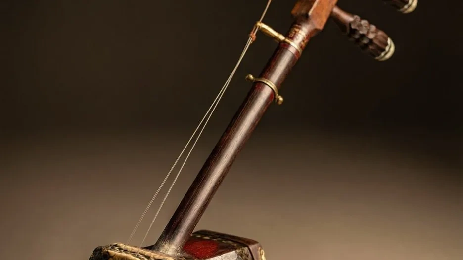 An erhu two-stringed fiddle with its python-skin sound box and long neck resting against dark silk, the horsehair bow laid alongside
