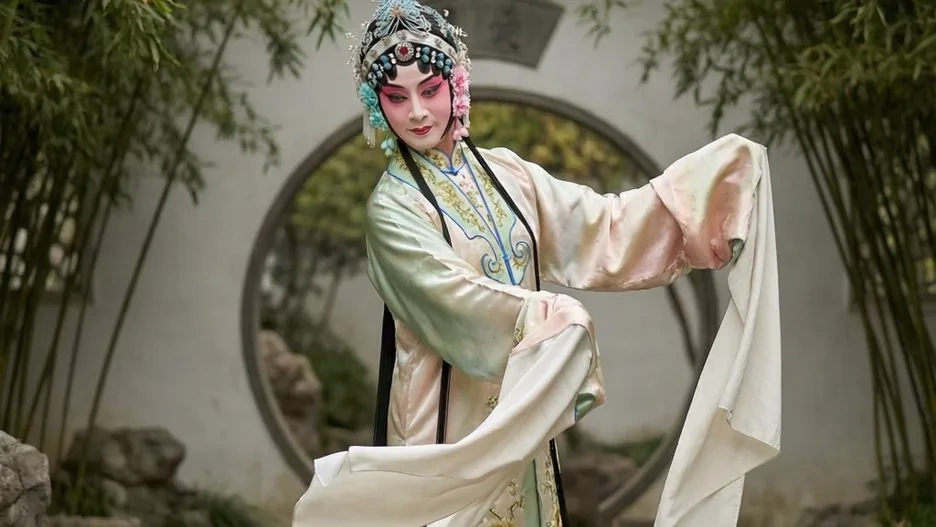 A Kunqu performer in flowing water sleeves and an ornate headdress, mid-gesture in a garden setting