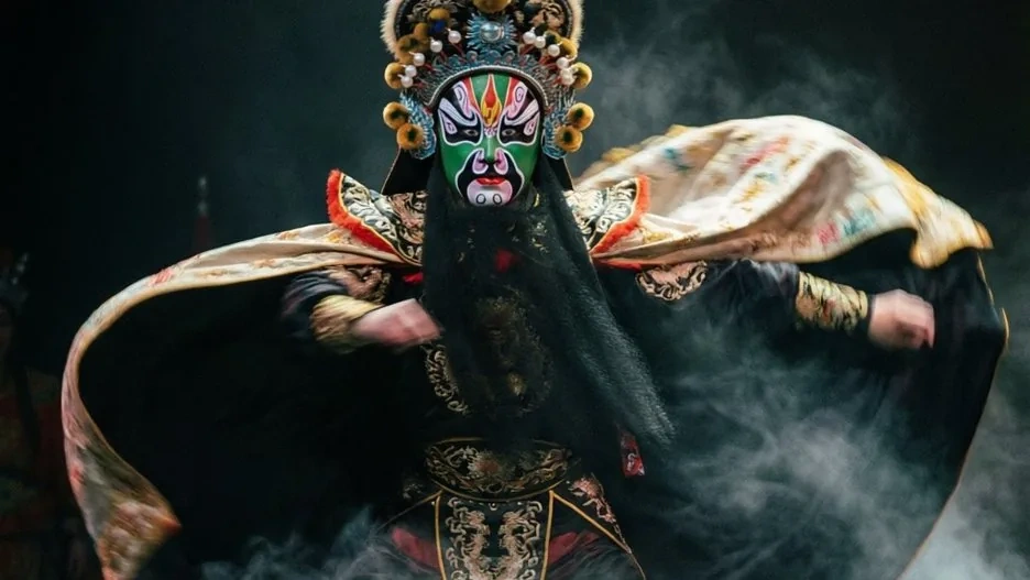 A Sichuan opera performer mid face-changing, vividly painted masks and swirling costume capturing the theatrical magic of Chuanju
